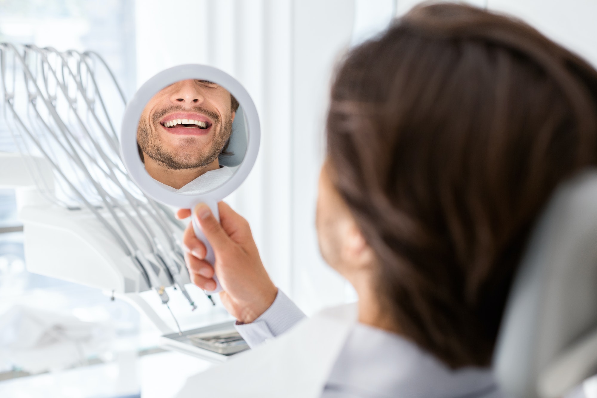 Satisfied patient checking smile at mirror in dental clinic